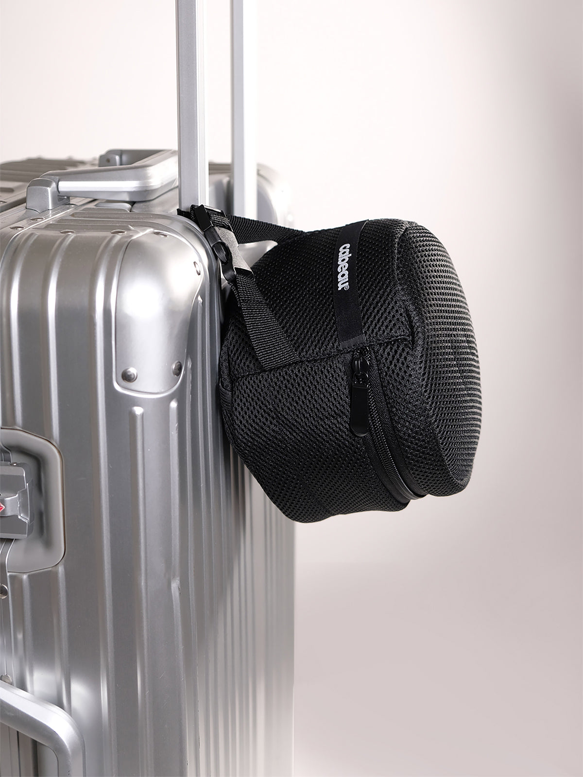 Black travel bag with neck pillow inside attached to a silver suitcase