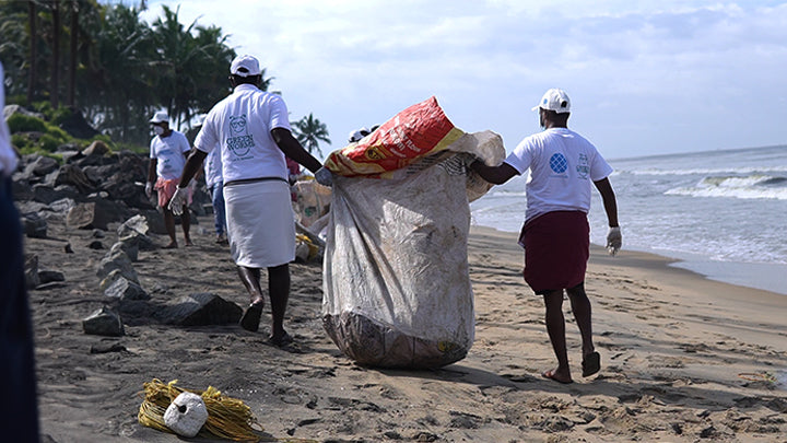 People participating in a beach clean-up activity with bags on a sandy beach.