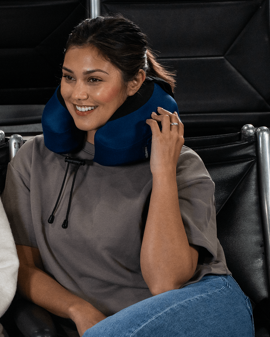 Woman sitting in an airplane terminal seat with a blue Evolution S3 neck pillow on